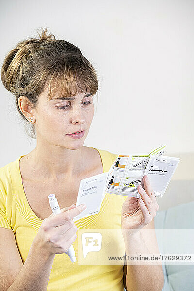 Diabetic woman reading the instructions for use of a kit to measure her sugar level and then inject herself with insulin.