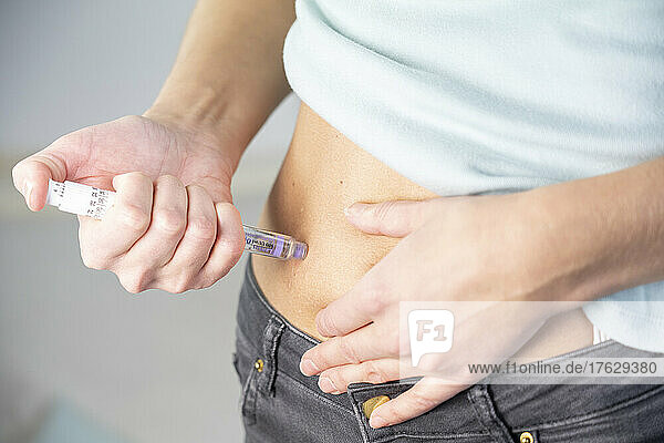 Close-up of the hands and stomach of a diabetic woman giving herself an insulin injection.
