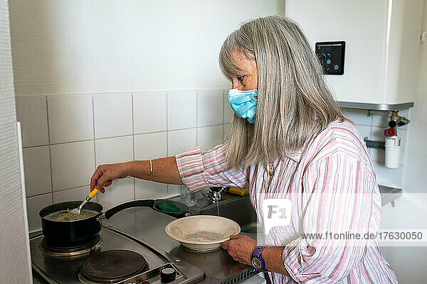 Caregiver in a retirement home looking after a septuagenarian with Parkinson's to do her cooking and cleaning.
