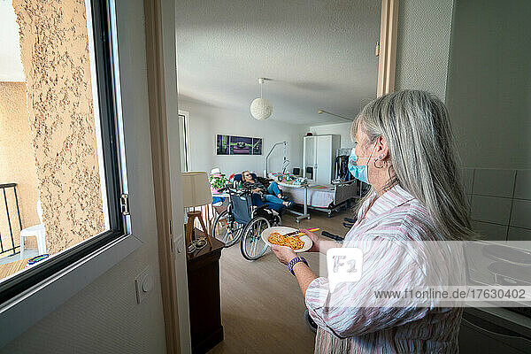 Caregiver in a retirement home looking after a septuagenarian with Parkinson's to do her cooking and cleaning.