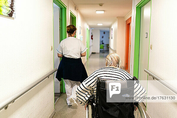 Centenary traveling in a wheelchair  assisted by a nursing assistant in an nursing home.