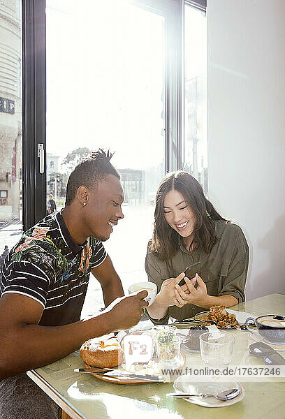 Smiling couple enjoying breakfast and looking at smart phone in restaurant