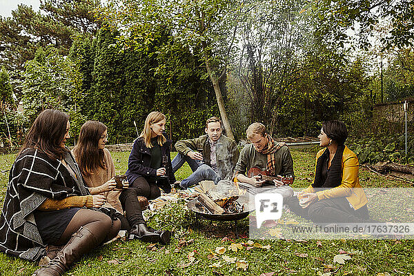 Group of friends having picnic around fire pit in garden
