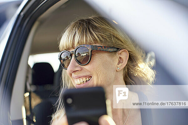 Mature woman in sunglasses using smart phone in car