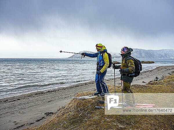 Bergführer deutet seinem Gast das nächste Ziel  Skitour endet am Strand  Senja  Troms  Norwegen  Europa