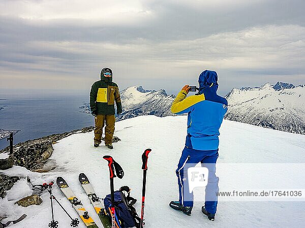 Skibergsteiger mit Handi macht ein Gipfelfoto auf dem Flobjörn mit Blick auf das Meer  Insel Senja  Troms  Norwegen  Europa
