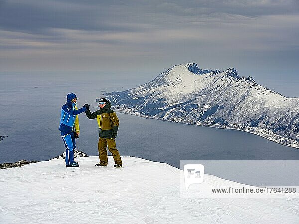 Two ski mountaineers congratulate each other at the summit of Flobjörn overlooking the Bergsfjord  Senja Island  Troms  Norway  Europe