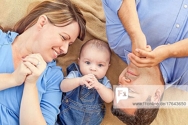 Junges gemischtrassiges Paar liegt mit seinem Kleinkind auf einer Decke