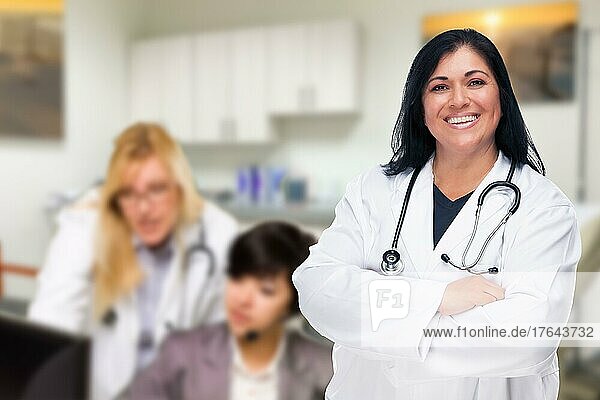Hübsche hispanische Ärztin oder Krankenschwester  die in ihrem Büro steht und deren Mitarbeiter dahinter arbeiten