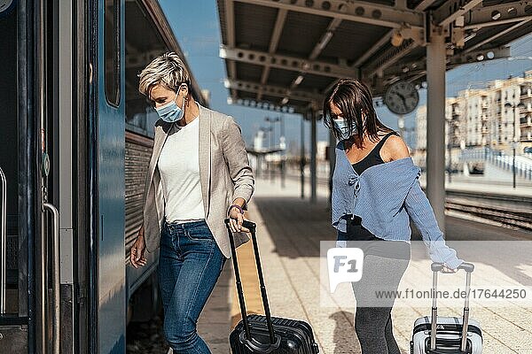 Two women in protective masks getting on the train with luggage