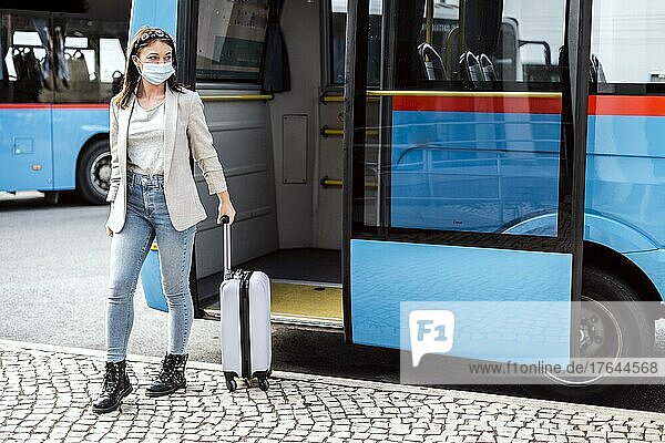 A young woman with mask and luggage has just left the bus after a long trip