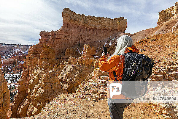 United States  Utah  Bryce Canyon National Park  Rear view of senior female hiker with backpack photographing rocks in Bryce Canyon National Park
