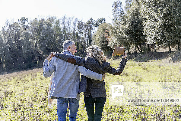 Mature couple walking with arms around on grassy land