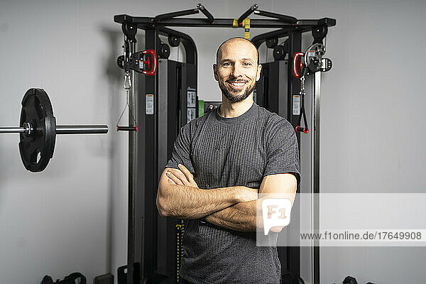 Smiling fitness instructor standing with arms crossed in front of exercise equipment at gym