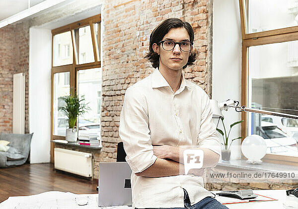 Businessman with arms crossed sitting on desk in office