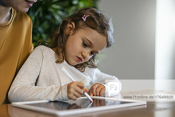 Nettes Mädchen  das zu Hause mit einem digitalisierten Stift auf einem Tablet-PC schreibt