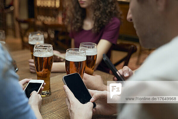 Friends having beer and using smartphones in a pub