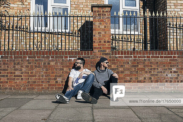 Two men sitting on sidewalk in front of brick wall