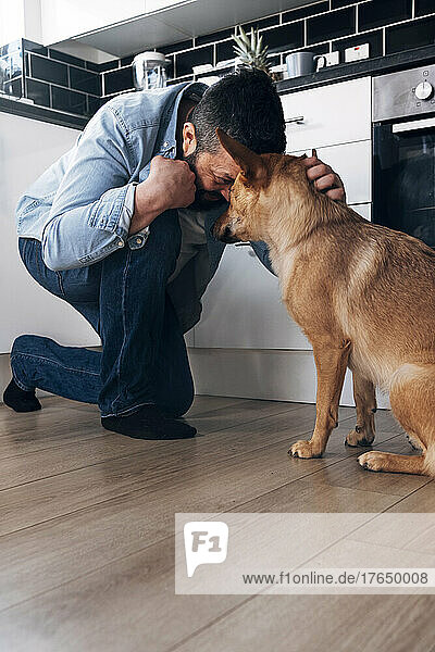 Verspielter Mann umarmt Hund in der heimischen Küche