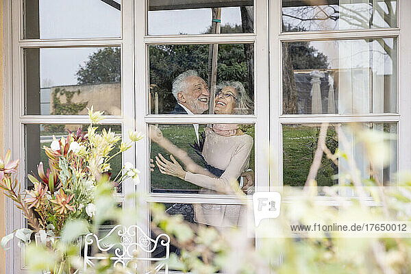 Happy senior couple embracing each other seen through window