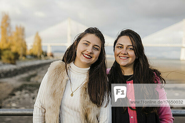 Happy women standing by railing in front of bridge