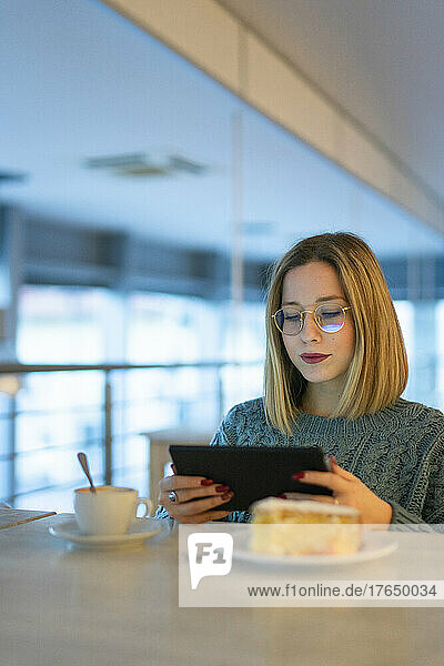 Junge Frau sitzt am Tisch und benutzt einen Tablet-PC
