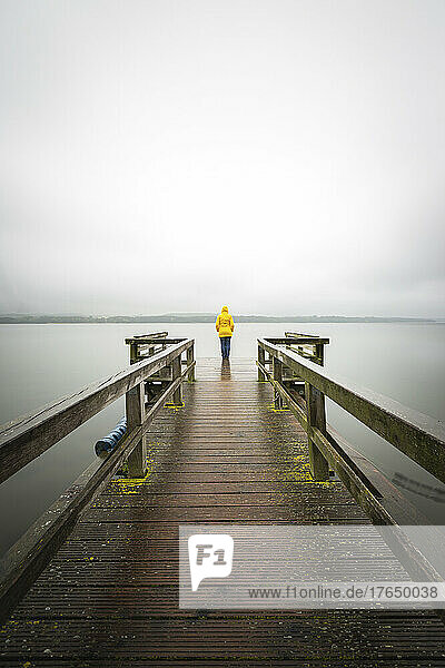 Germany  Schleswig-Holstein  Woman in yellow jacket standing on edge of lakeshore jetty