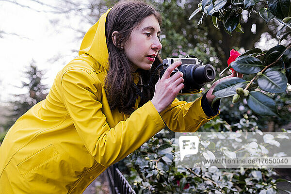 Young woman photographing flower through camera in forest