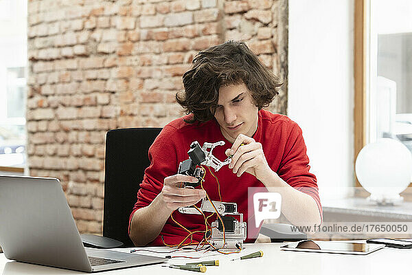 Teenager arbeitet an einem kleinen Roboterarm und sitzt mit einem Laptop am Tisch