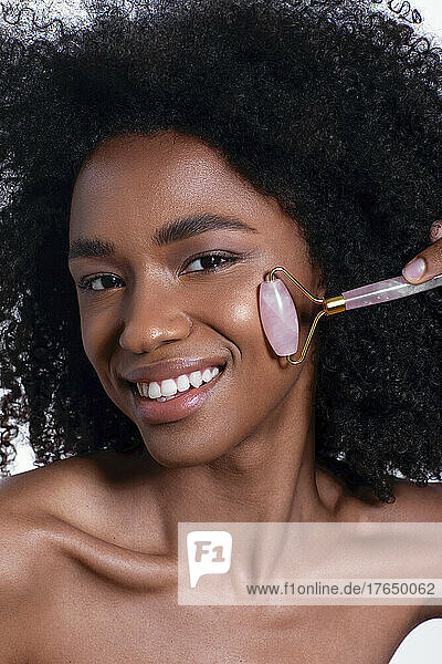 Smiling young woman giving facial massage with quartz roller