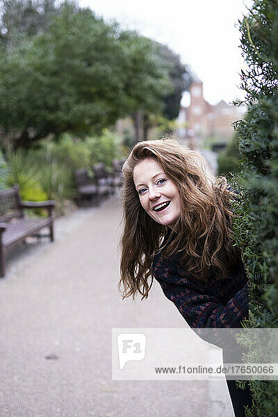 Happy young woman peeking behind plant at park