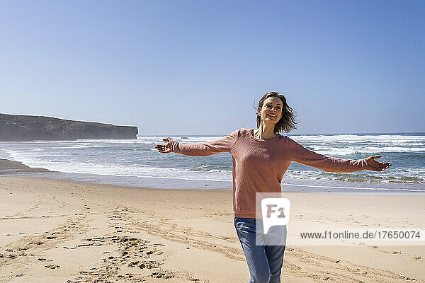 Carefree woman with arms outstretched enjoying sunny day at beach