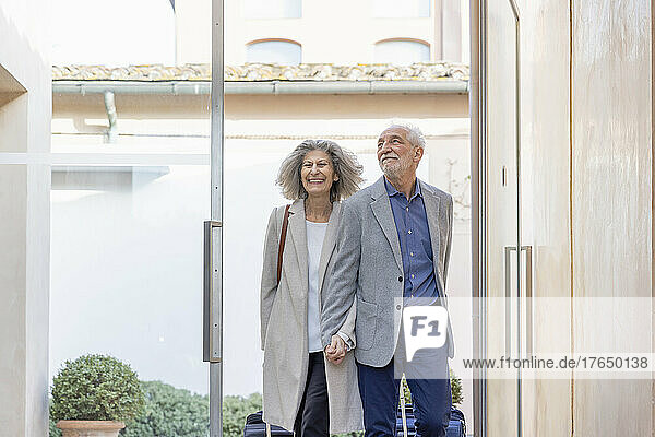 Happy senior couple holding hands arriving at boutique hotel