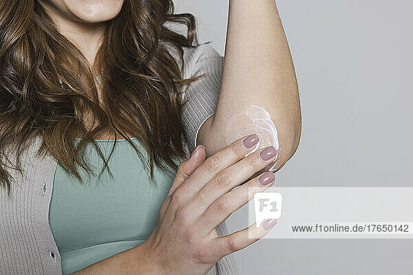 Hand of woman applying cream on elbow against gray background