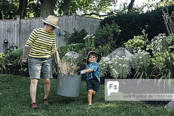 Grandmother with grandson carrying basket of plant together in garden