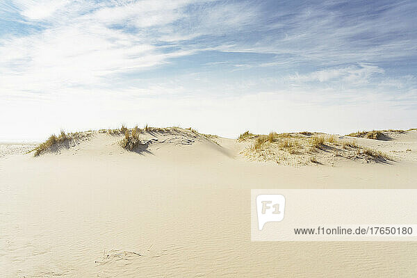 Sand dunes under cloudy sky on sunny day