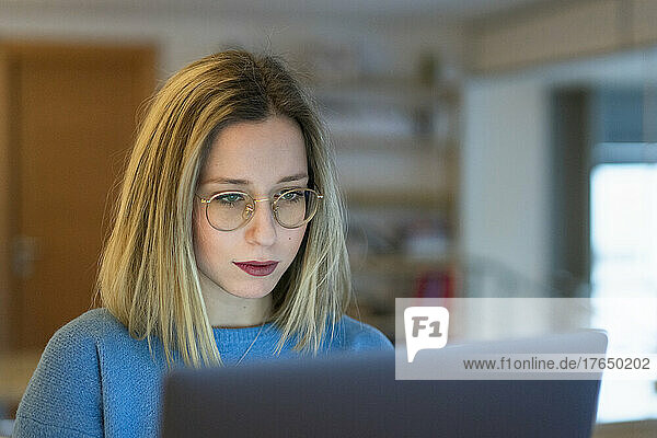 Young blond woman using laptop sitting at table