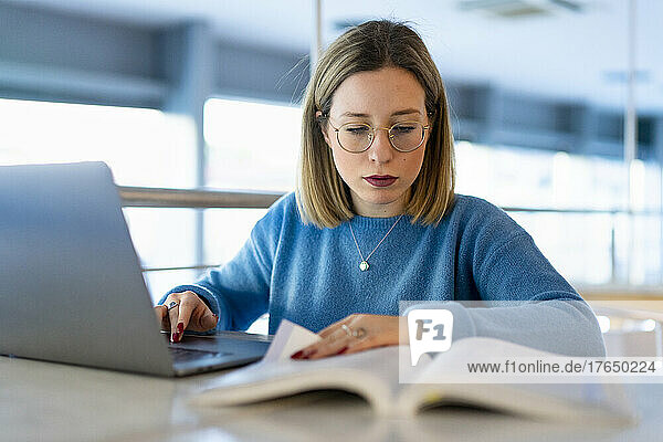 Young woman with laptop and book studying at table