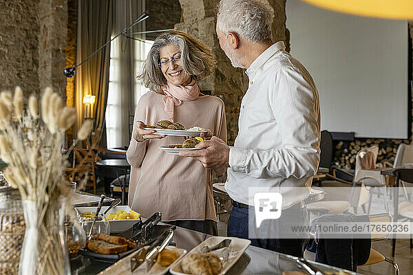 Happy senior couple enjoying breakfast at buffet in boutique hotel