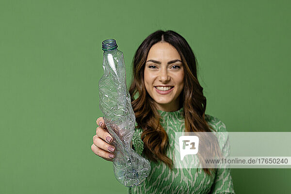 Smiling young woman showing plastic bottle against green background