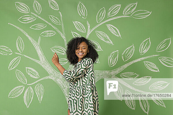 Lächelnde Frau steht vor einem Baum und zeichnet auf eine grüne Wand