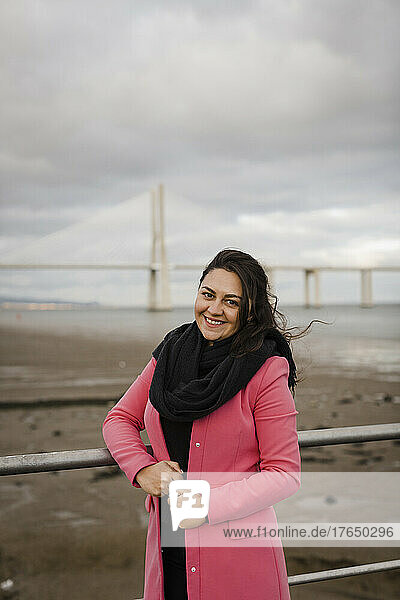 Smiling woman standing by railing in front of bridge