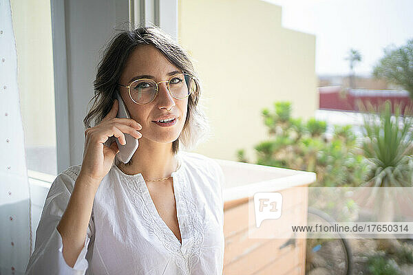 Junge Frau mit Brille telefoniert zu Hause
