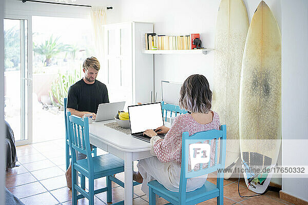 Freelancers using laptops sitting at dining table working from home