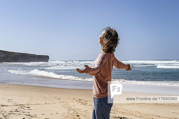 Carefree woman with arms outstretched enjoying at beach on sunny day