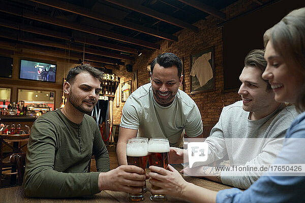 Freunde treffen sich in einer Kneipe und stoßen mit Biergläsern an