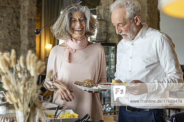 Glückliches älteres Paar mit Tellern  die am Frühstücksbuffet im Boutique-Hotel stehen
