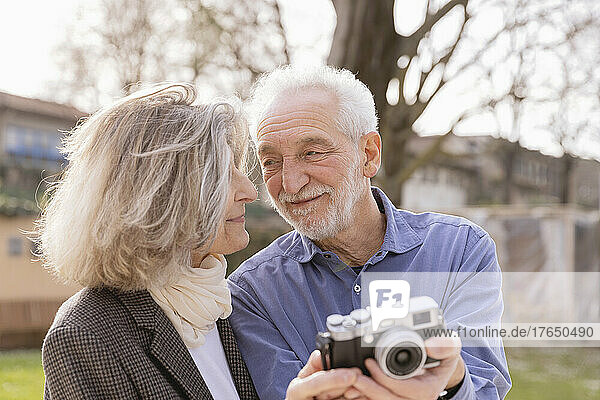 Happy senior couple with camera looking at each other on sunny day