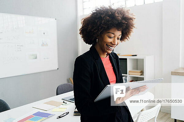 Happy young businesswoman with Afro hairstyle using tablet PC in office