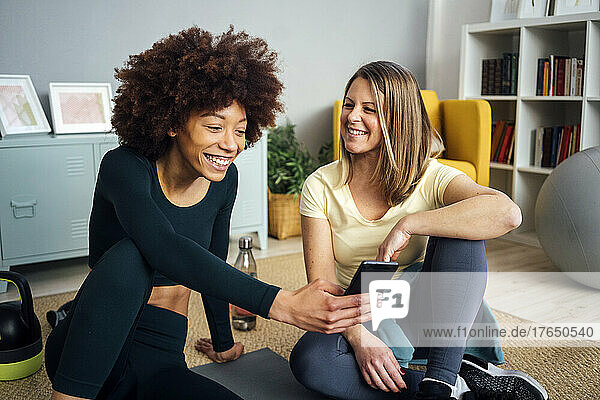 Happy bond woman looking at friend using smart phone in living room